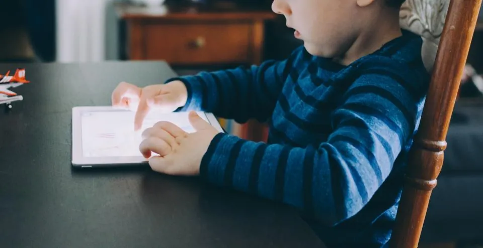 Dziecko w wieku wczesnoszkolnym korzysta z tabletu przy stole