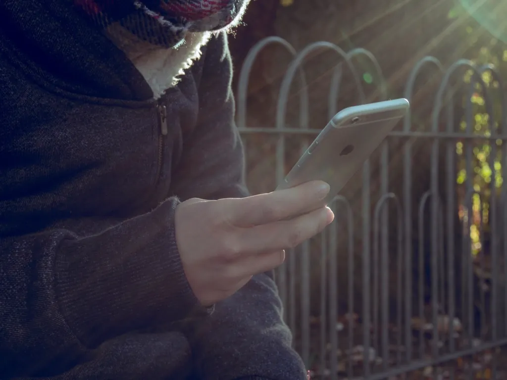 Młoda osoba w kapturze przewija telefon – dopaminowa pętla nagrody